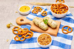 Oktoberfest set. White sausage weisswurst, pretzels, mustard, spikelets of grain, hop. Traditional German cuisine, festival food. Bowls, linen napkin, stone concrete background close up