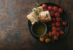 Traditional italian Appetizer home made foccacia bread served with olive oil and baked tomatoes and rosemary over a rustic wooden background. Top View